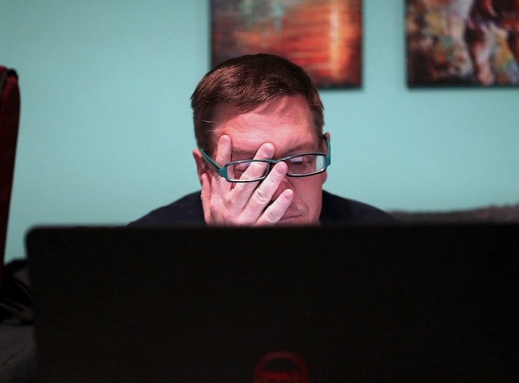 ein Mann sitzt müde am Rechner und reibt sich die Augen